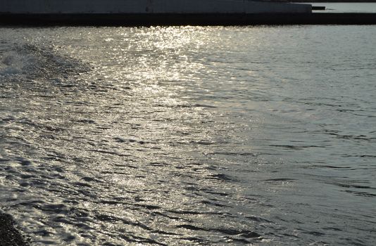 Shiny silver water on the sea pebble beach, early morning sunrise.