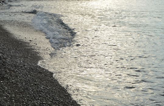 Shiny silver water on the sea pebble beach, early morning sunrise.