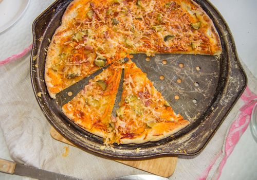 Top view of freshly baked appetizing homemade pizza on a metal pan with cheese and ham, close-up food background.