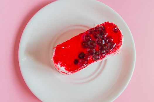 Exquisite souffle cake with lingonberry jelly, with berry glaze and coconut on a white plate, top view close-up, pink background.