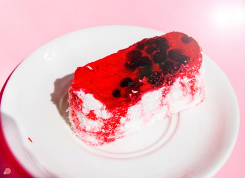 Exquisite souffle cake with lingonberry jelly, with berry glaze and coconut on a white plate, top view close-up, pink background.