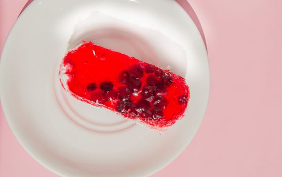 Exquisite souffle cake with lingonberry jelly, with berry glaze and coconut on a white plate, top view close-up, pink background.