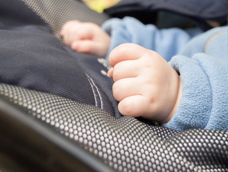 Hands of a baby fist, selective focus, the child is in the stroller.