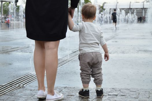 child's mother stood together holding hands in the Park in the summer, look at the fountain. The view from the back. The concept of unity and care