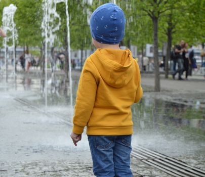 child standing near a puddle in the Park near the fountain, watching the water jets.