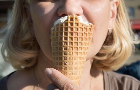 Outdoor closeup of a woman eating a delicious ice cream in a waffle cone with pleasure in hot weather.