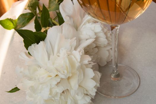 White wine in the glass and peony flowers. Romantic dinner.