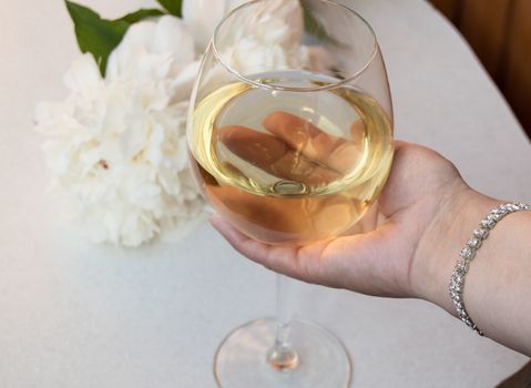 glass of white wine holding woman's hand in the bracelet. Closeup