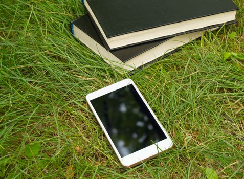 Books, smartphone on a green grass background, concept of education and training.