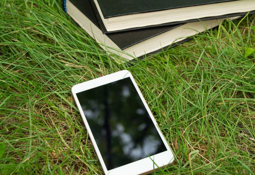 Books, smartphone on a green grass background, concept of education and training.