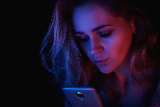Girl using cellphone at night with neon light - pink and blue and black background