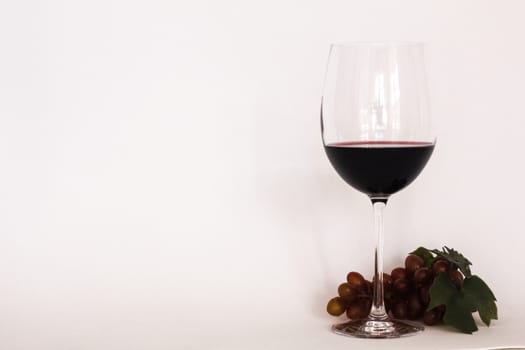 Glass of red wine vith a bunch of grapes and white background