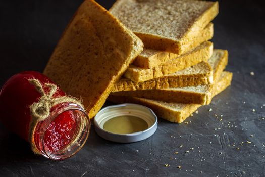 Strawberry jam bottle and whole wheat bread are stacked on a black background. Concept of breakfast and healthy food.