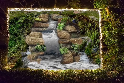 River water splashing on the rocks on billboard in a hedge edged with a string of lights.