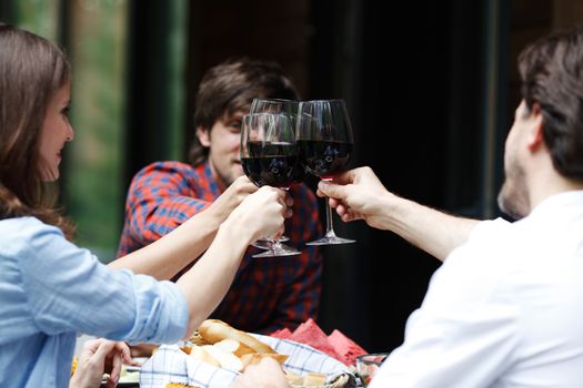 Friends clink glasses of red wine at outdoor dinner