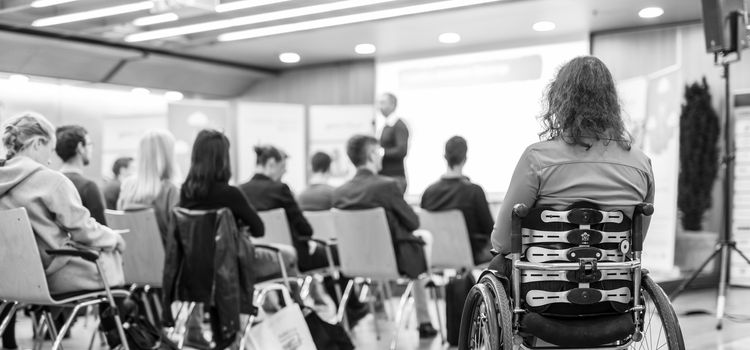 Rear view of unrecognizable woman on wheelchair participating in business conference talk. Business and entrepreneurship symposium. Black and white image.