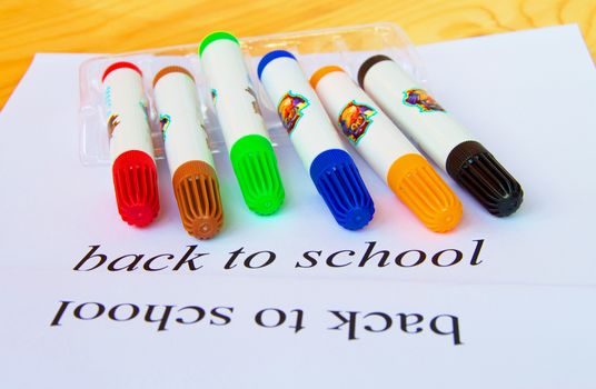 Back to school. A sheet of paper with text and colored markers on a wooden background, selective focus.