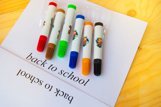 Back to school. Sheet of paper with text and colored markers on a wooden background, top view.