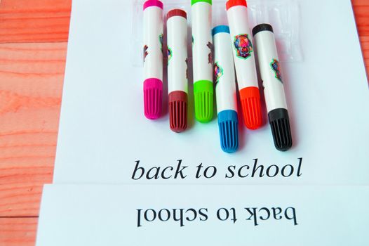 Back to school. Sheet of paper with text and colored markers on a wooden background, top view.