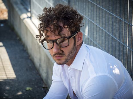 One handsome man in urban setting in European city, sitting against metal grid