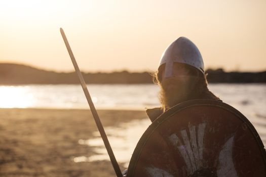 Portrait of slavic warrior reenactor with sword and shield posing outdoors at seaside