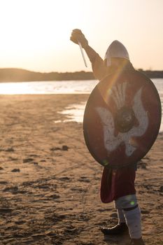 Portrait of slavic warrior reenactor with sword and shield posing outdoors at seaside