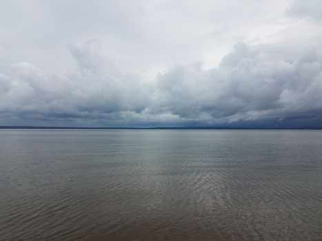rain clouds forming over calm river water near shore