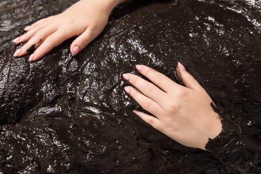 The female hand lies on black therapeutic mud