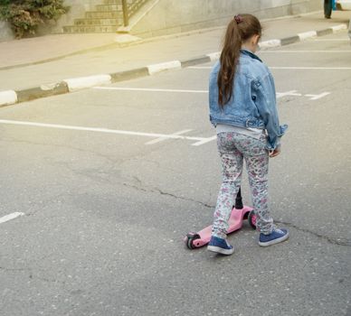 Little girl in a denim jacket walks down the street to ride scooter