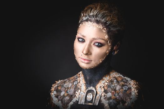 Portrait of a blue eyed young girl with creative golden makeup in the style of icon painting isolated on black background