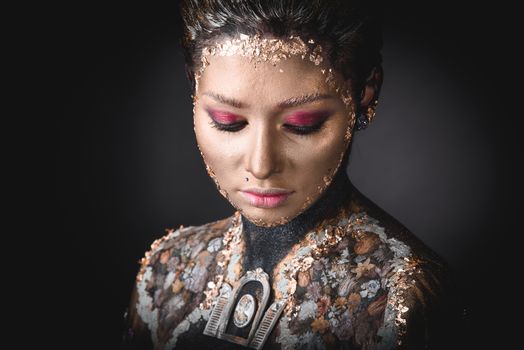 Portrait of a blue eyed young girl with creative golden makeup in the style of icon painting isolated on black background