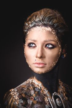 Portrait of a blue eyed young girl with creative golden makeup in the style of icon painting isolated on black background