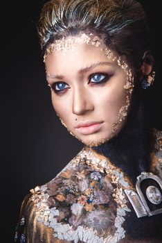 Portrait of a blue eyed young girl with creative golden makeup in the style of icon painting isolated on black background