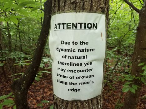 attention warning about erosion sign on tree in woods or forest
