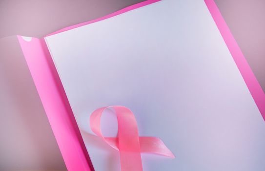 Pink ribbon on a sheet of paper to raise awareness of breast cancer, copy space, top view.