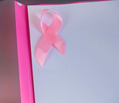 Pink ribbon on a sheet of paper to raise awareness of breast cancer, copy space, top view.