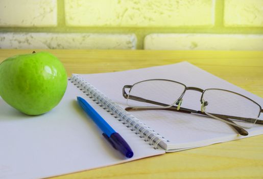 Teacher's Day concept and back to school, green Apple, book, laptop, reading glasses and pen on wooden table, sunlight.