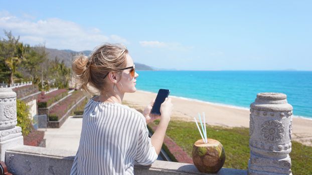 A beautiful young woman on a tropical beach with a phone in her hands. Rest, vacation, resort, beautiful life
