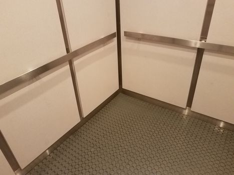 interior of elevator or lift with grey floor and metal bars and white walls