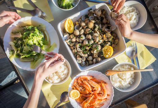 A few people are enjoying a seafood meal with some vegatables and rice.