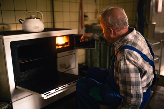 Old man putting coal in to the stove in the cottage