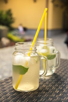 Super icy lemonade on wooden table with lemon and a leaf of mint with straw in summer.