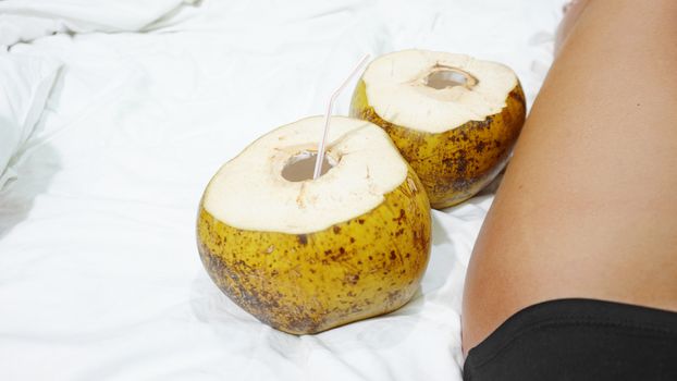 Female bare feet on a white sheet, top view, closeup. Coconut cocktail near the feet. Hotel by the sea concept