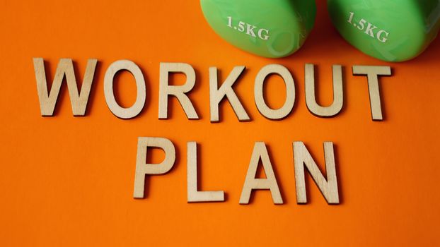 Fitness concept, workout plan. Green dumbbells on orange background. Top view. Flat lay
