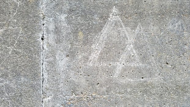 grey cement wall with two triangles scratched or drawn on the surface