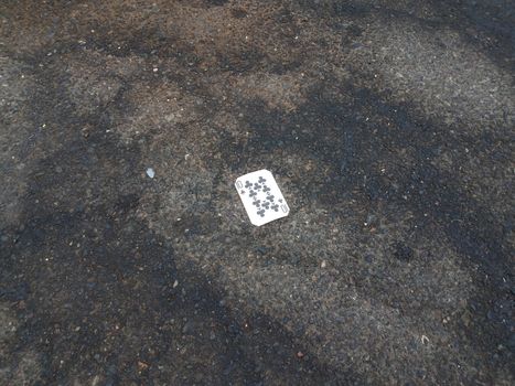 ten of clubs playing card on black asphalt or pavement