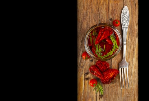 Delicious dried tomatoes in the jar of olive oil, the fork on wood background. In rustic style. With a space for text.