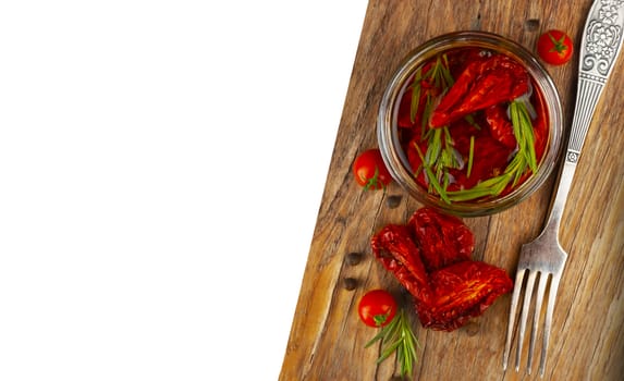 Delicious dried tomatoes in the jar of olive oil, the fork on wood background. In rustic style. With a space for text.