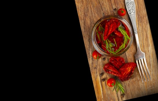 Delicious dried tomatoes in the jar of olive oil, the fork on wood background. In rustic style. With a space for text.