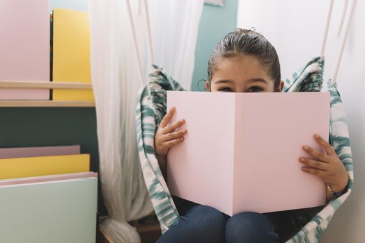 sweet happy little girl reading a book in her room near the window, funny lovely child having fun in kids room